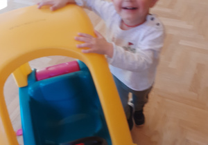 Na zdjęciu roześmiany chłopiec wsiadający do zabawkowego pojazdu.