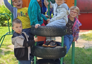 Na zdjęciu uśmiechnięta grupa dzieci na urządzeniu na placu zabaw.