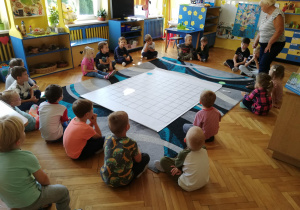 dzieci siedzą na dywanie, przed nimi mata do kodowania z zaznaczonymi kropkami