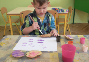 Chłopiec w koszuli maluje ziemniaka farbą