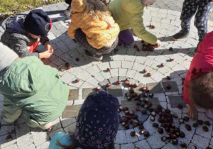 Na zdjęciu dzieci układające schemat budowy drzewa z kasztanów