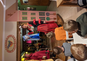 Na zdjęciu widać aktorów z Baśniowej Kawiarenki prezentujących lalki biorące udział w spektaklu Śpiąca Królewna i dzieci z grupy VI siedzące na widowni