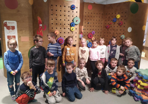 Dzieci z grupy piątej pozują na tle ściany z kolorowymi kołami zębatymi