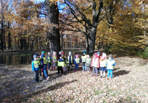 dzieci przy parkowym stawie oglądają otaczającą je przyrodę jesienią