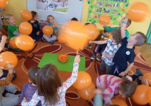 Na zdjęciu dzieci bawiące się w sali przedszkolnej pomarańczowymi balonami.