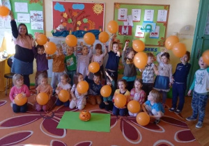 Na zdjęciu grupa dzieci wraz z nauczycielką pozują z pomarańczowymi balonami.