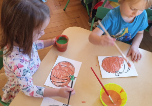 na zdjęciu dzieci malujące kontury dyni rosnącymi farbami.