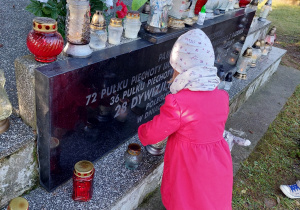 na zdjęciu dziewczynka w różowym płaszczu stawiająca znicz na grobie