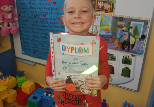 Zdjęcie przedstawia szczęśliwego chłopca z grupy VI, który pokazuje dyplom i nagrody za I miejsce w konkursie plastycznym pt " Jeż to super zwierz"