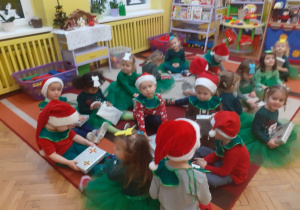 Na zdjęciu dzieci siedzące na dywanie oglądają prezenty otrzymane od Świętego Mikołaja.