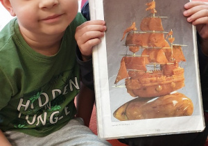 Na zdjęciu dwa chłopcy pozują ze zdjęciem przedstawiającym statek z bursztynów.