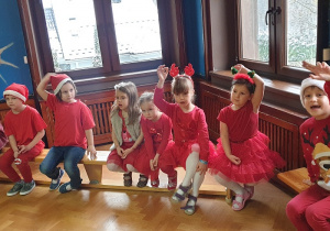 Na zdjęciu dzieci ubrane na czerwono podnoszą ręce i zgłaszają się do konkursu