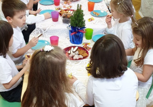 na zdjęciu grupa dzieci siedząca przy stole z przysmakami.