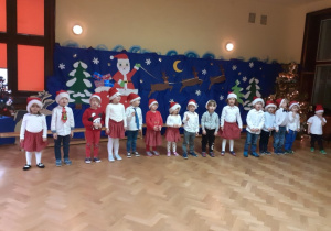 Dzieci uroczyście ubrane stoją na tle świątecznej dekoracji