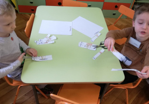 Dzieci przy stolikach wycinają puzzle i naklejają w odpowiednim ułożeniu na kartce