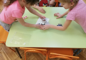 Dzieci przy stolikach w małych zespołach układają puzzle na czas​