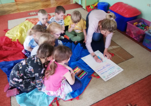 Dzieci siedzą na dywanie, gdzie wymyślają swój plan na wymarzony dzień w przedszkolu, nauczycielka zapisuje pomysły na dużym kartonie