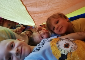 Dzieci leżą pod chusta animacyjną zaczepionej na małych krzesełkach w formie namiotu