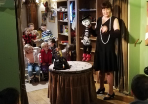 Aktorka prezentuje lalkę :Kota w butach", w tle dzieci patrzące na lalkę .