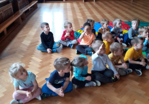 Na zdjęciu dzieci siedzące na podłodze na sali gimnastycznej.