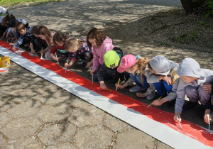 Na zdjęciu dzieci kucające przy długim pasie papieru, malujące go na narodowe barwy.