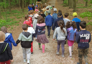 Na zdjęciu grupa dzieci idąca leśną drogą za przewodnikiem.