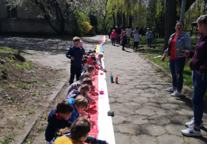 dzieci na przedszkolnej alejce malują farbami na długiej płachcie papieru polską flagę
