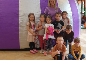 Na zdjęciu dzieci z nauczycielką przed biało fioletową kopułą kina sferycznego