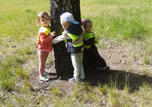 Na zdjęciu troje dzieci obejmuje drzewo.