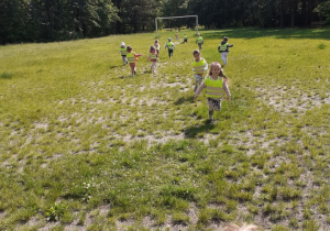 Na zdjęciu grupa przedszkolaków biega po boisku w parku.