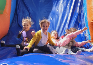 Na zdjęciu grupa dzieci zjeżdżających z dmuchanej zjeżdżalni