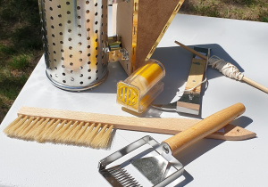Na zdjęciu narzędzia używane przez pszczelarza, między innymi: podkurzacz, szczotka do pszczół, łąpacz królowej