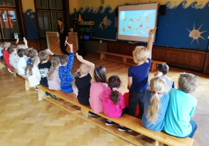dzieci na sali przed tablica multimedialna, prowadzącą zajęcia objaśnia z pomocą projekcji na tablicy multimedialnej działanie japońskiego liczydła oraz zadaje dzieciom proste zagadki matematyczne