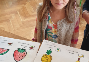 Zdjęcie przedstawia dziewczynkę z pokolorowanymi ilustracjami owoców