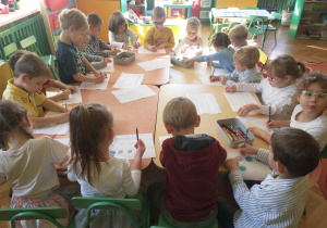 dzieci z gr 3 rozwiązują karty pracy przy wspólnym stole