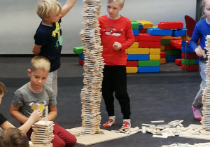 na zdjęciu dzieci budujące wieże i inne konstrukcje z drewnianych klocków Linden. Między dziećmi widać ogromna ilość drewnianych klocków