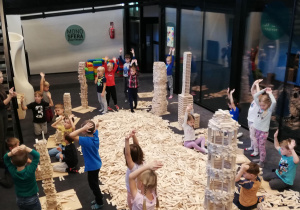 na zdjęciu dzieci budujące wieże i inne konstrukcje z drewnianych klocków Linden. Między dziećmi widać ogromna ilość drewnianych klocków