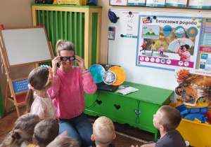 Na zdjęciu nauczycielka pokazuje okulary przez które można oglądać zjawisko zaćmienia słońca.