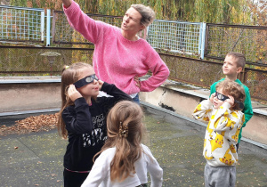 Na zdjęciu czworo dzieci i nauczycielka wskazująca gdzie na niebie szukać zjawiska zaćmienia.