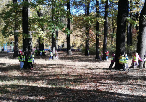 Na zdjęciu dzieci w grupach 3-4 osobowych przytulają się do drzew w parku.