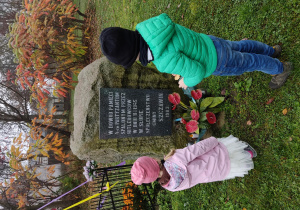Dziewczynka i chłopiec stoją przy miejscu pamięci w którym spalono czterech partyzantów przez Hitlerowców w Słupie