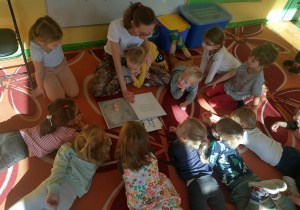 Dzieci leżą na dywanie w kole słuchając książki
