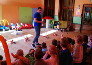 Na zdjęciu stojący przed siedzącymi dziećmi prelegent objaśniający dzieciom działanie drukarek 3D.
