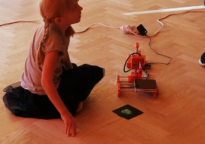 Na zdjęciu dziewczynka kuca przy małej drukarce 3D.