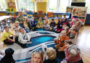 dzieci siedzą na dywanie w klasie , pokazuja swoje pluszakowe zwierzątka
