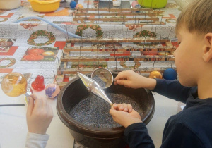 Dzieci przedszkolne w dekoratorni bombek. Z wielkim zaangażowaniem samodzielnie dekorują swoje bombki wykorzystując do tego kolorowe brokaty i klej.
