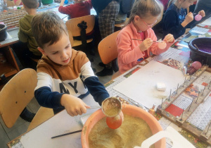 Dzieci przedszkolne w dekoratorni bombek. Z wielkim zaangażowaniem samodzielnie dekorują swoje bombki wykorzystując do tego kolorowe brokaty i klej.