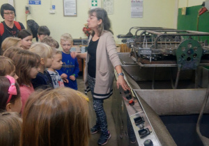 Przedszkolaki przebywające w pomieszczeniu w którym znajdują się maszyny do suszenia bombek z zaciekawieniem słuchają cennych informacji na temat produkcji i dekoracji bombek.