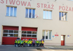 Grupa dzieci przedszkolnych stoi przed budynkiem Państwowej Straży Pożarnej.