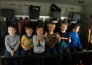 Uśmiechnięte dzieci przedszkolne pozują do zdjęcia siedząc w aucie strażackim.